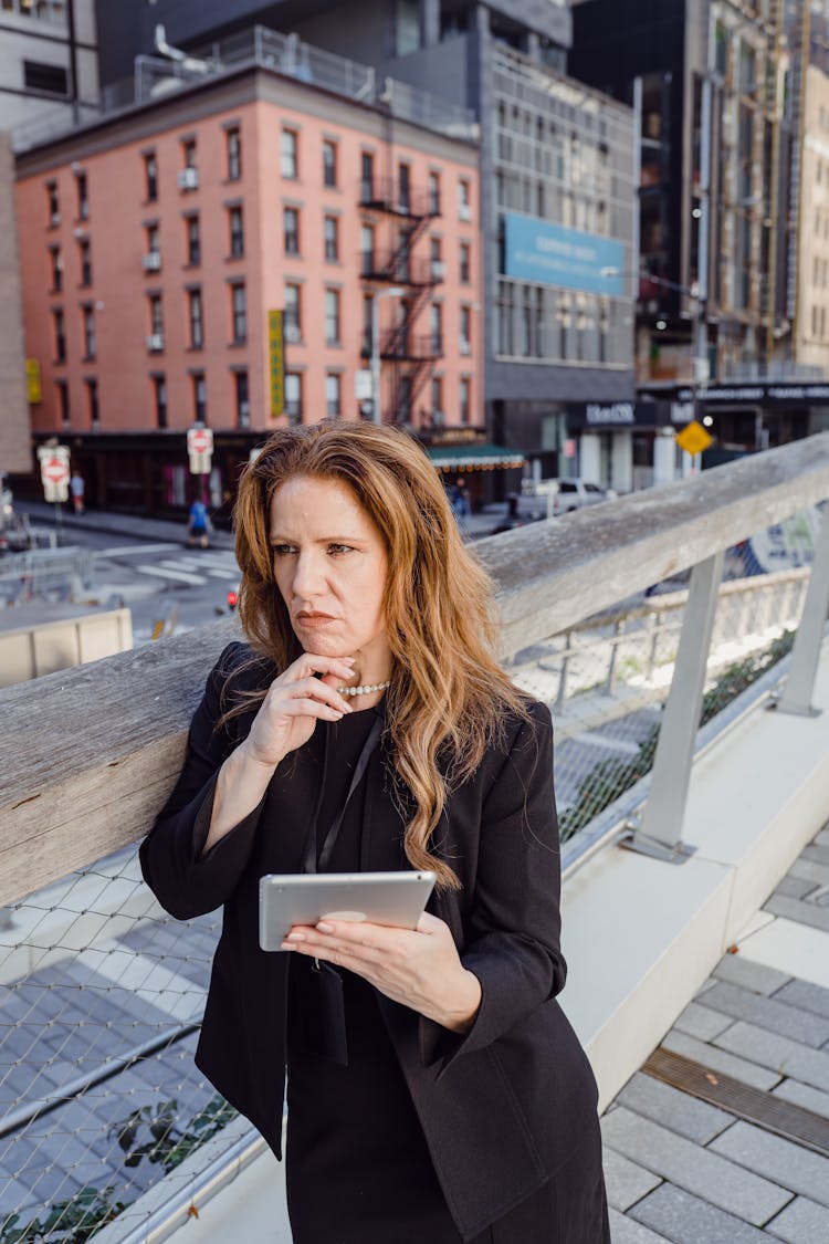 Businesswoman Leaning Against Railing In A City And Calculating Business Risk