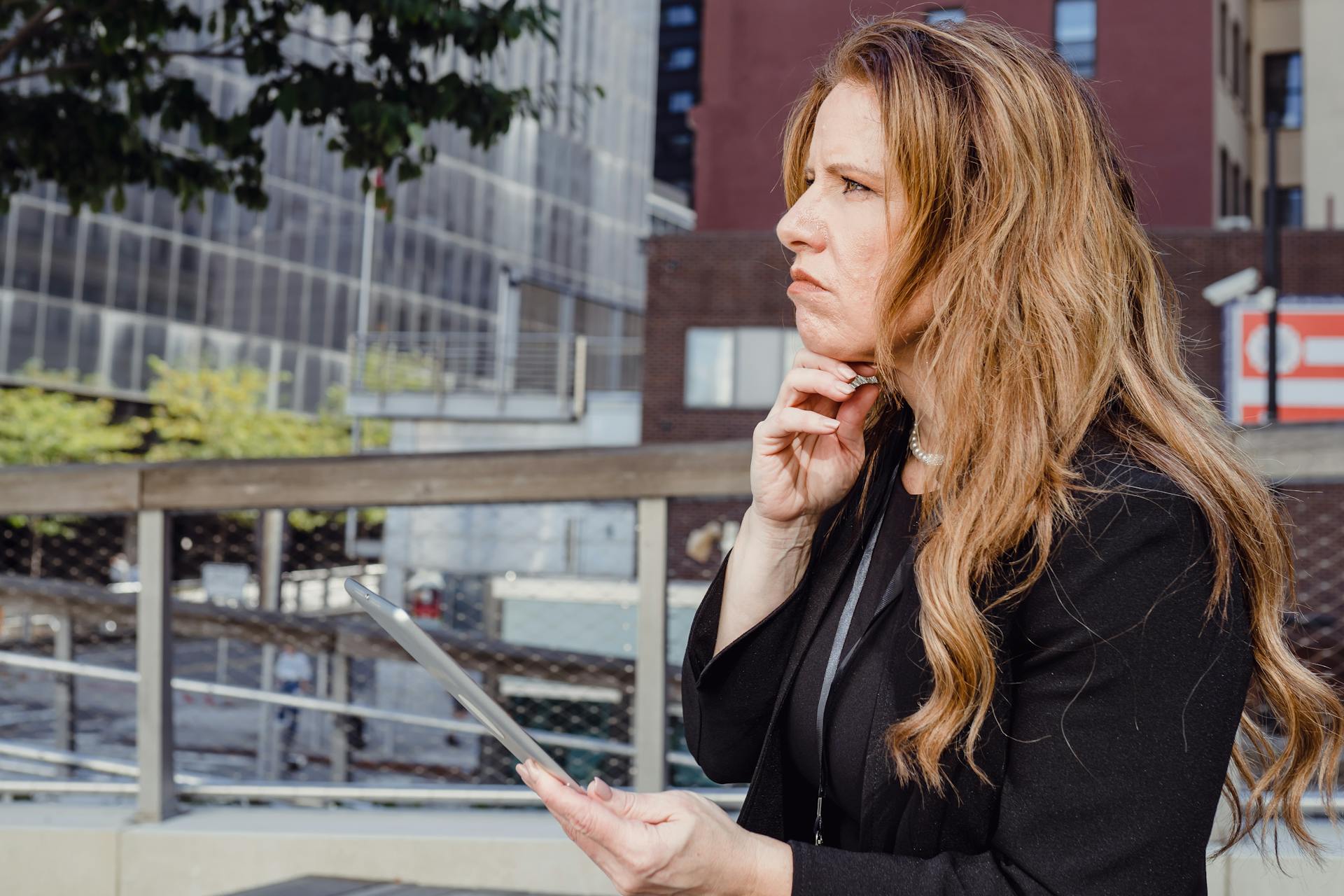 A businesswoman with long hair uses a tablet in an urban setting, showcasing modern technology and business concepts.