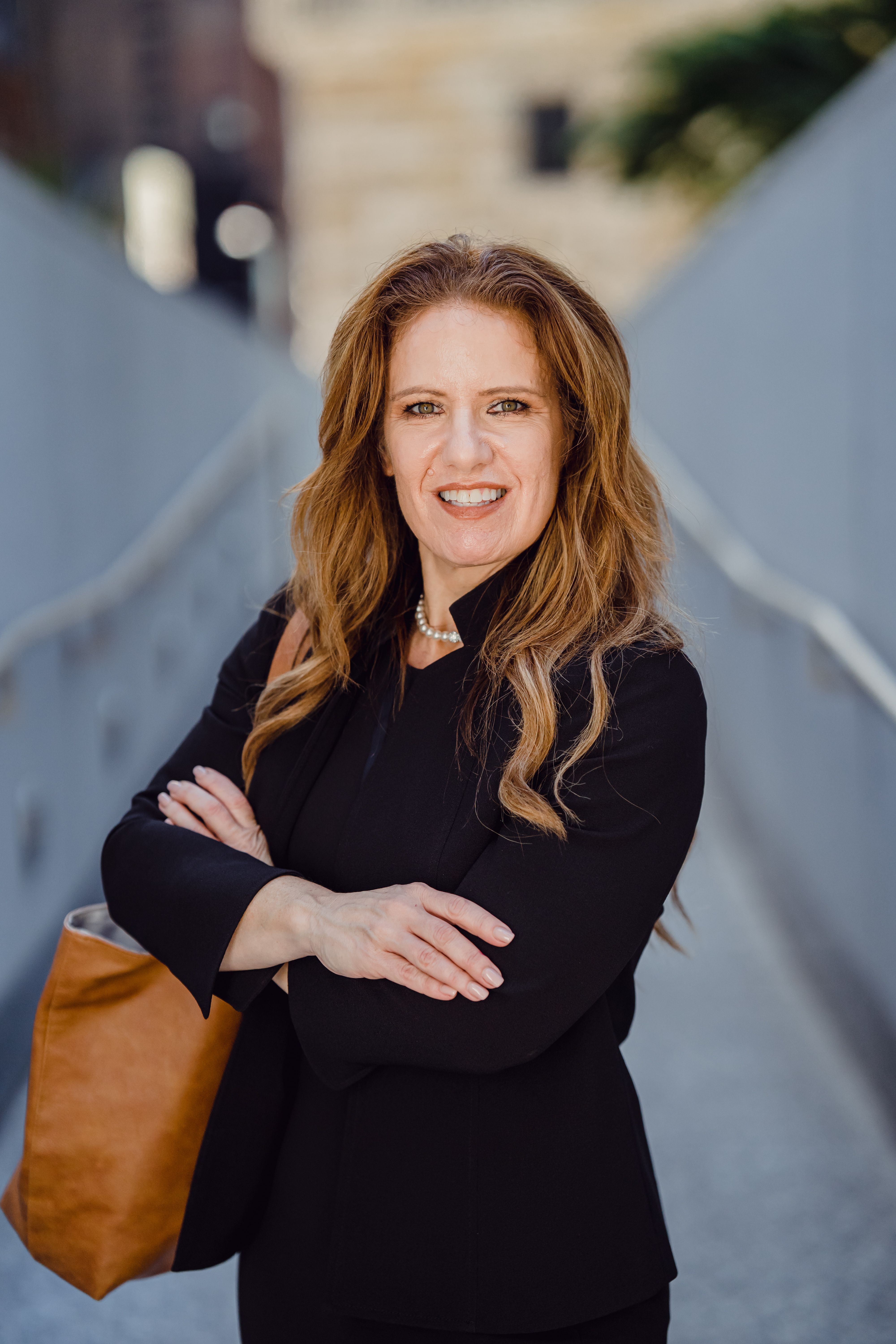 Portrait of a confident businesswoman smiling in an urban setting, wearing a black suit.