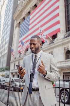 African American businessman on a city street near the New York Stock Exchange, using a smartphone.