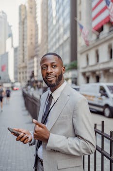 Smiling businessman in a suit using a smartphone on a bustling city street.