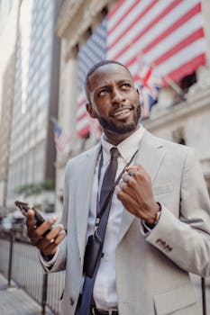 A businessman in a gray suit celebrates success while holding a smartphone outdoors.
