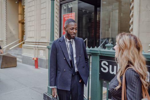 Businessman and woman talking in the city, near a subway entrance.