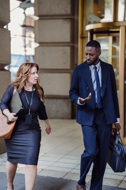 Free Two business professionals engaged in conversation while walking outside an office building. Stock Photo