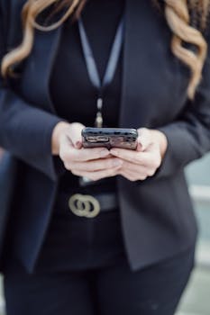 Close-up of a woman holding a smartphone, dressed in a black business suit, showcasing modern technology.