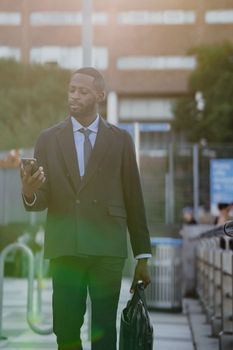 Confident businessman in a suit using a smartphone while walking outdoors with a briefcase.