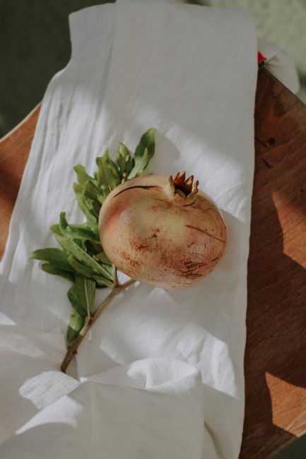 A pomegranate with greenery on white fabric, capturing natural freshness.
