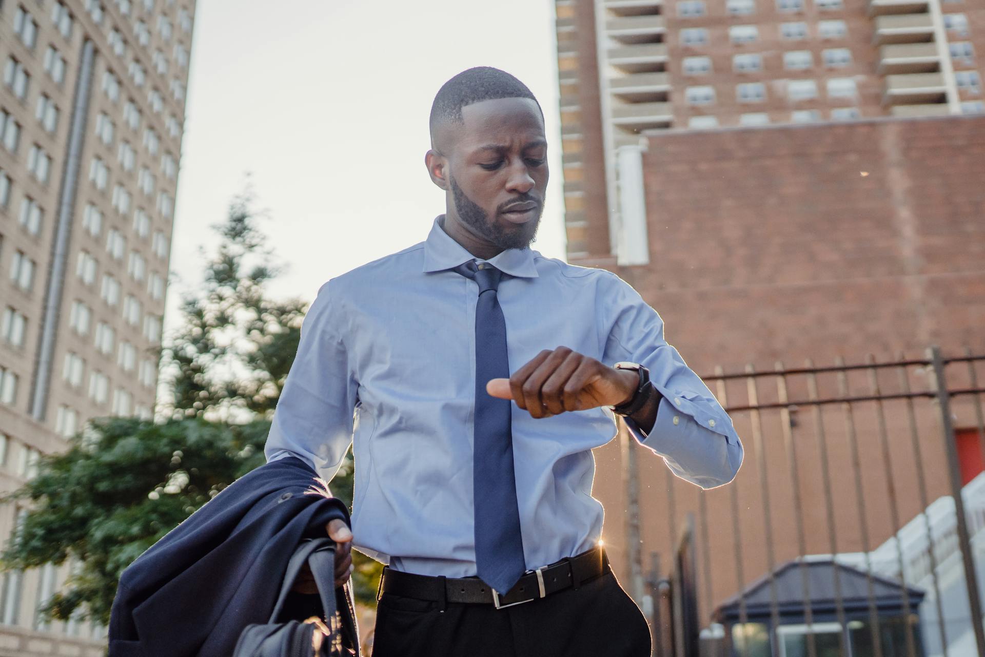 Young professional checks watch in a city backdrop, conveying urgency and business lifestyle.