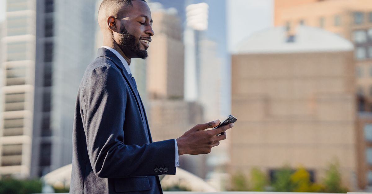 Businessman in a suit using a smartphone outdoors in a city with modern architecture