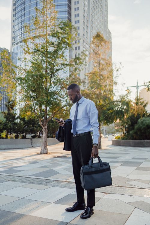 Free Professional man in cityscape, checking phone and holding briefcase, during daytime. Stock Photo