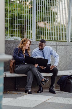 Two diverse business professionals reviewing documents outdoors on a bench.