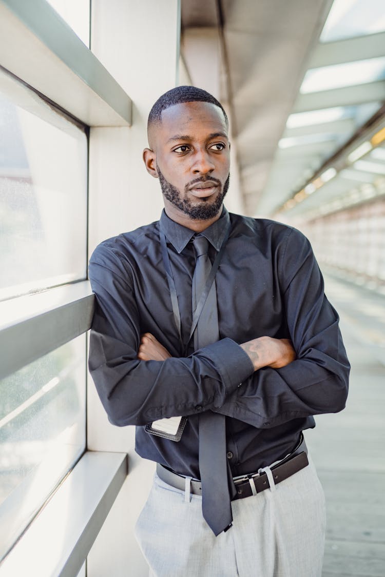 Man In Business Attire Leaning On A Window With His Arms Crossed