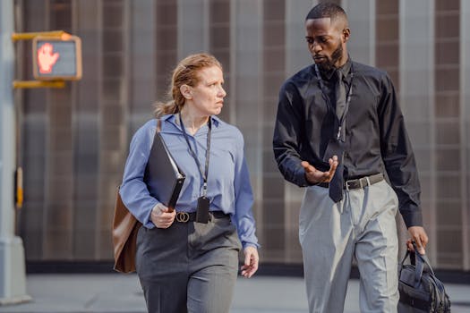 Two professionals in business attire walk and discuss outside a modern building.