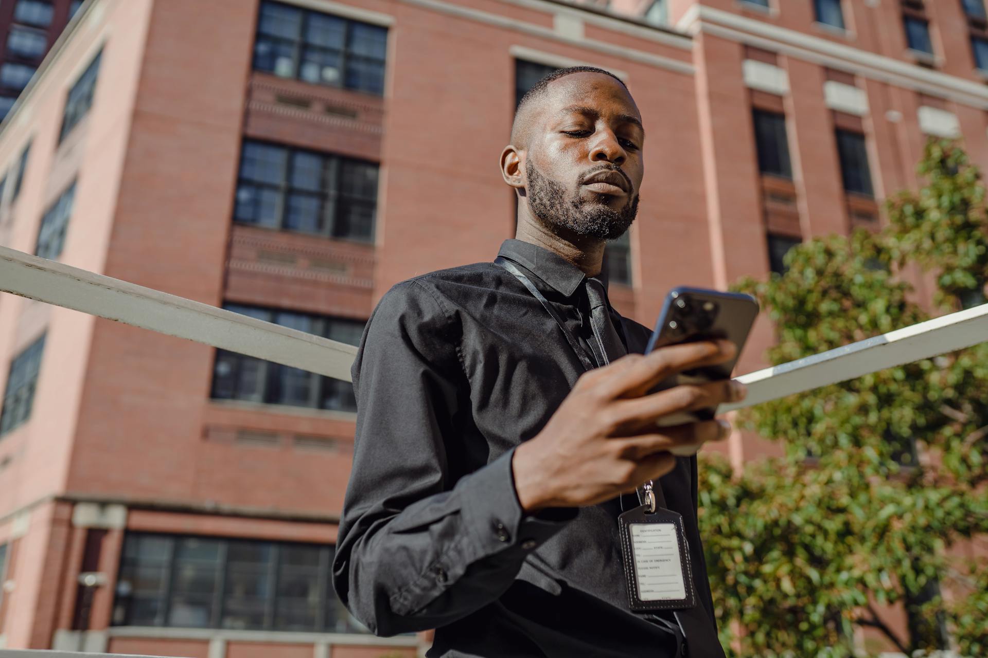 Professional man in business attire using smartphone outside office building during the day.