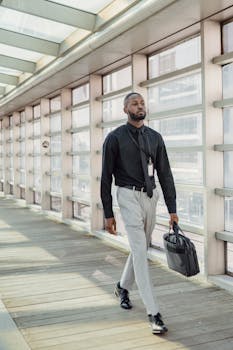 Confident business professional walking in a glass-covered hallway holding a laptop bag.
