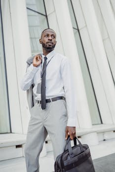 A professional man in business attire holding a laptop bag in front of a modern building.