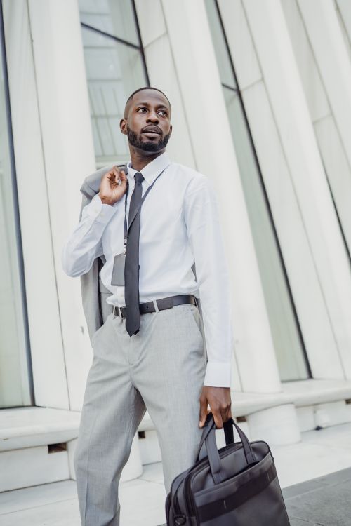 Free A professional man in business attire holding a laptop bag in front of a modern building. Stock Photo