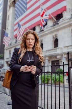 Professional woman texting on smartphone with flags in background, city setting.