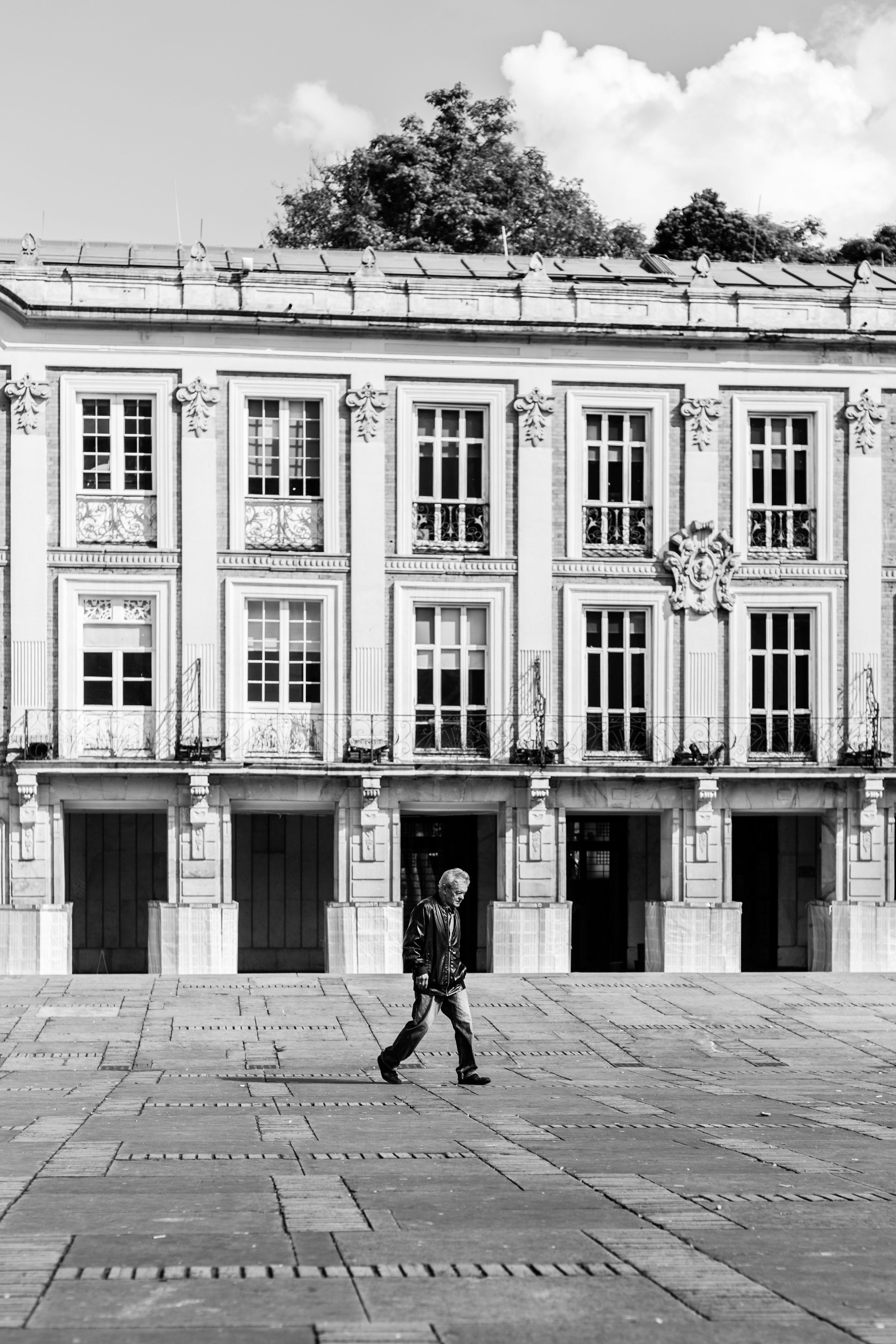 Black and white street scene of a man walking by a historic building in Bogotá, Colombia.