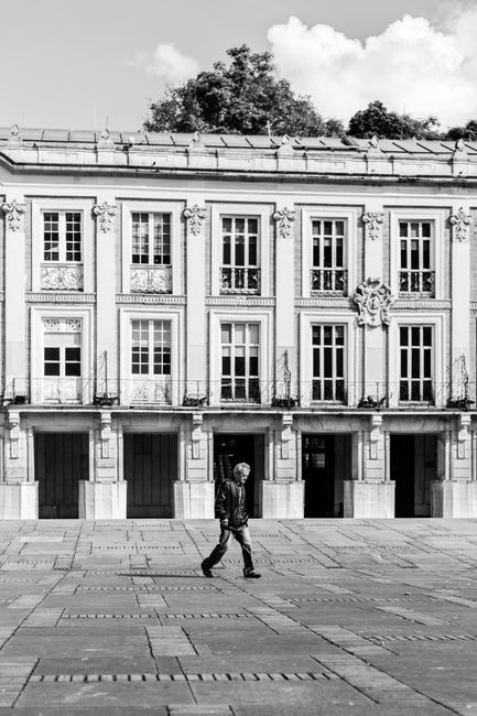 Black and white street scene of a man walking by a historic building in Bogotá, Colombia.