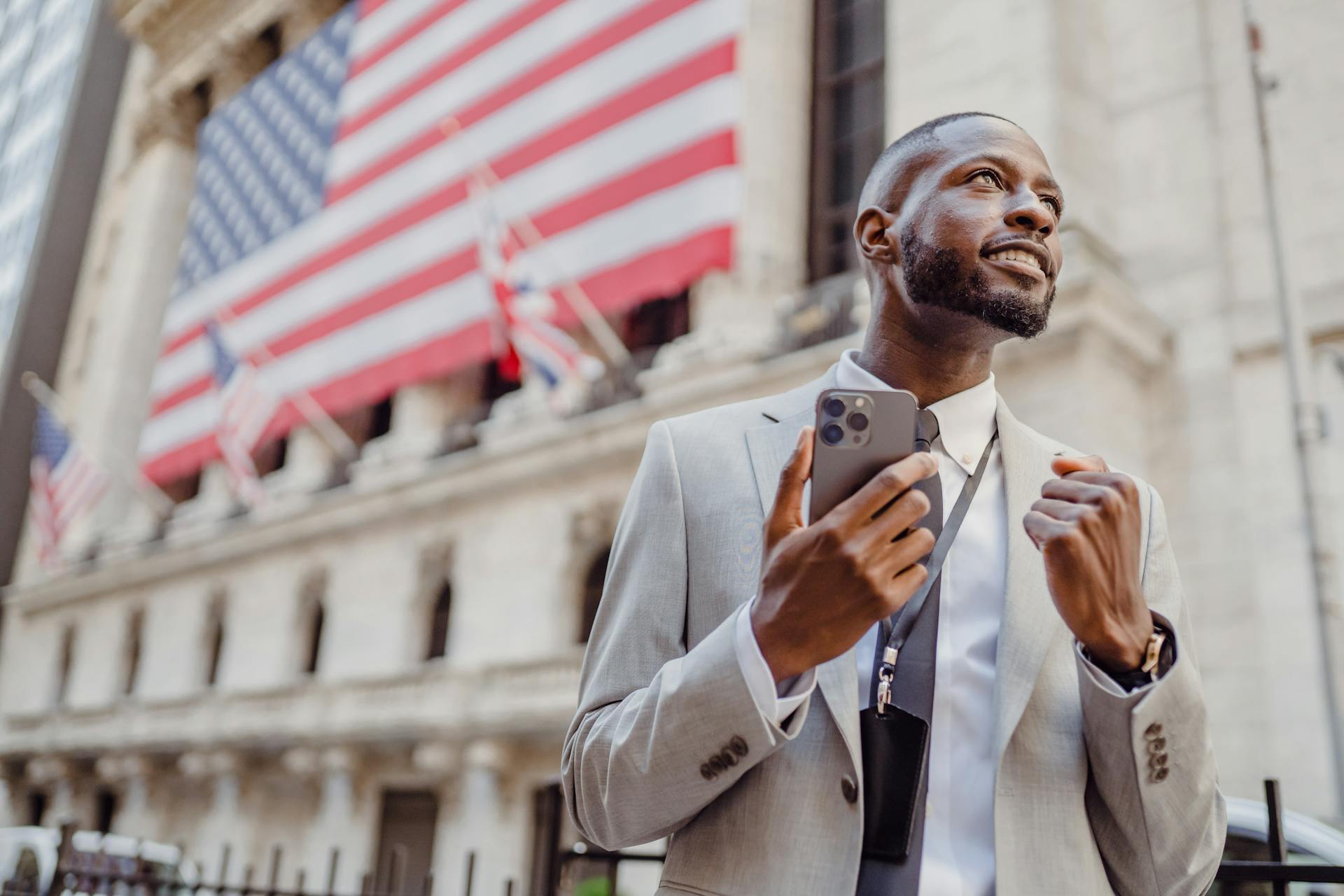 Confident businessman with phone in front of Wall Street building with American flags.