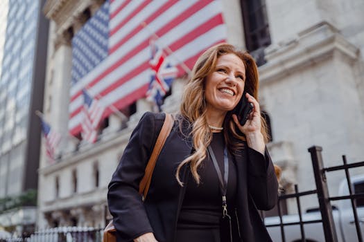 Smiling businesswoman using phone outside the stock exchange with flags in background.