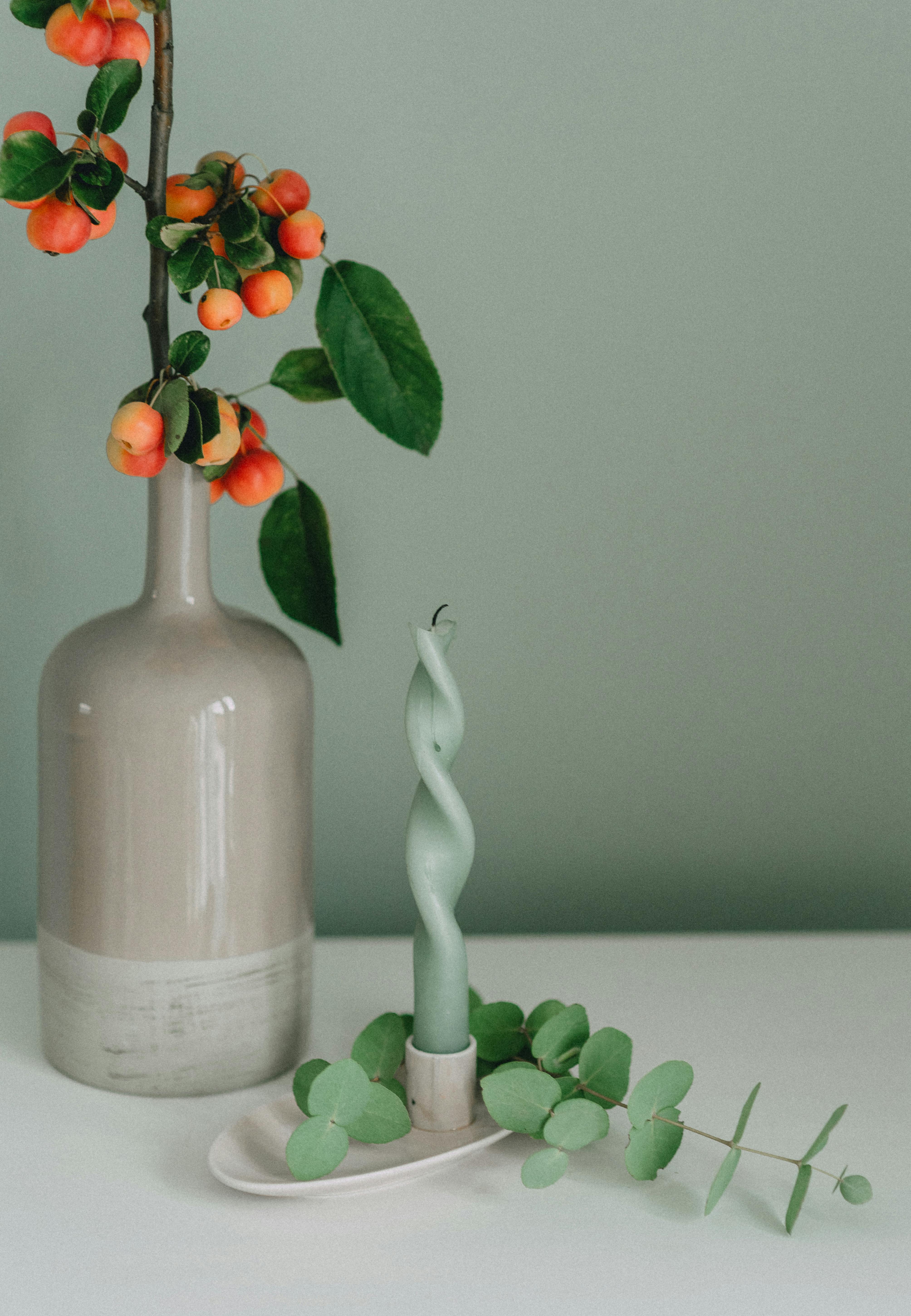 A minimalist photo featuring a green twisted candle on white surface with a ceramic vase.