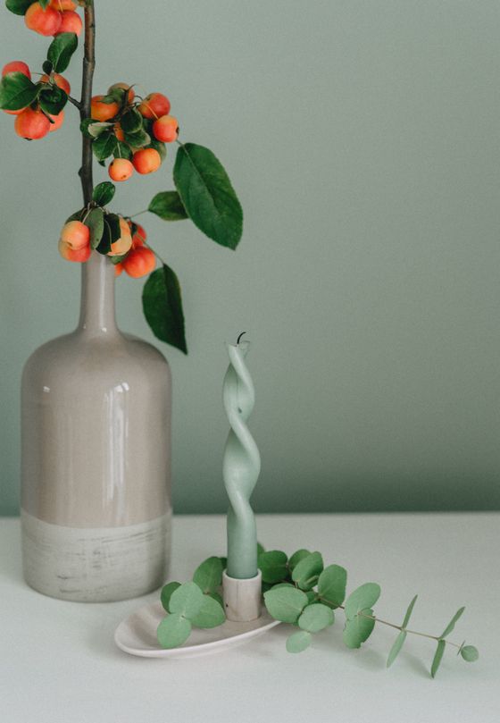 Ceramic bottle and taper candle against sage green, photo by Lara on Pexels