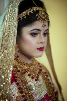A South Asian bride elegantly dressed in traditional bridal attire with intricate jewelry and makeup.