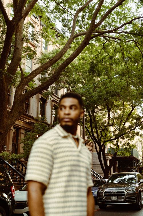 Free Blurred man in striped shirt on city street with trees and buildings. Stock Photo