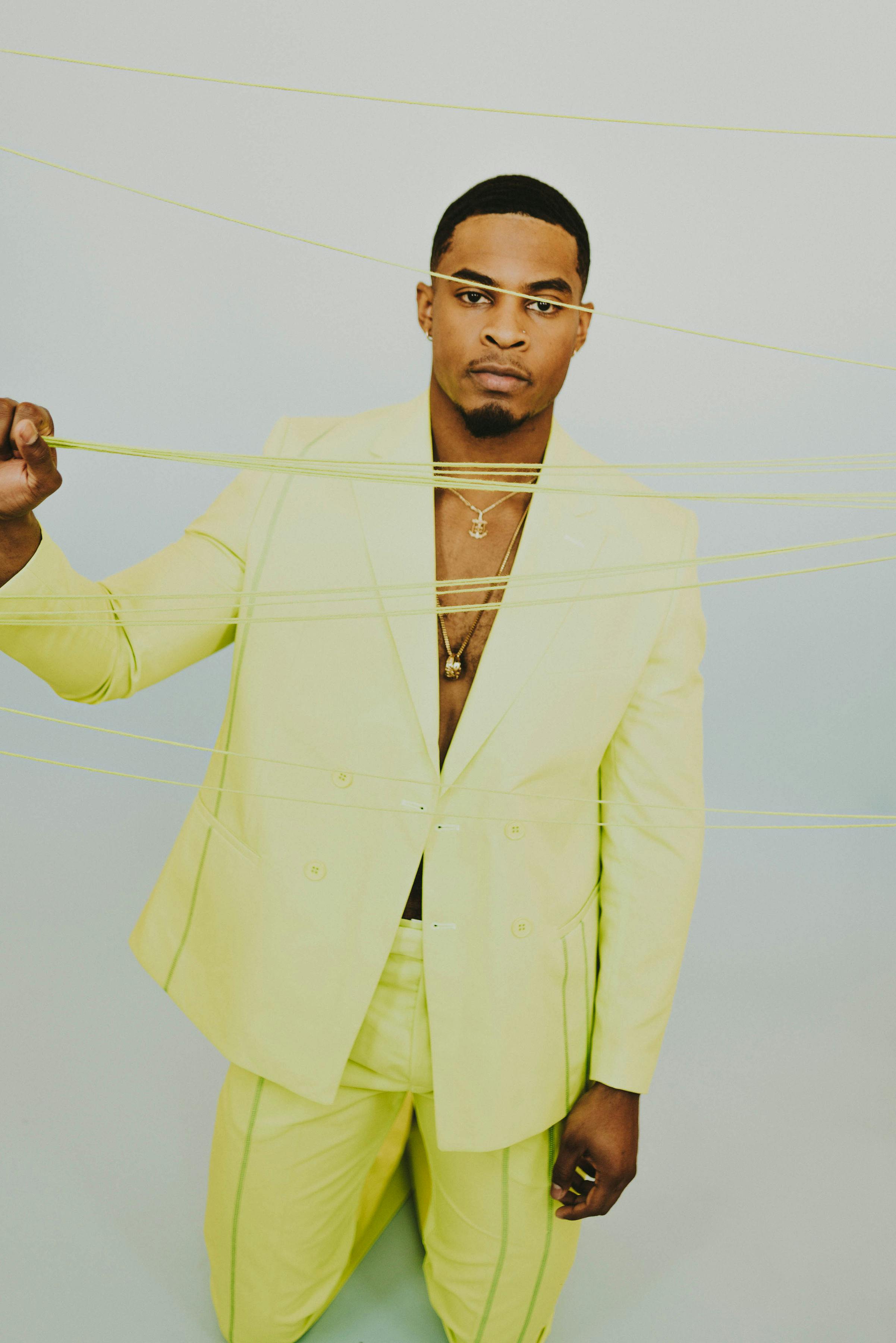 Portrait of a fashionable man in a yellow suit posing creatively with strings indoors.