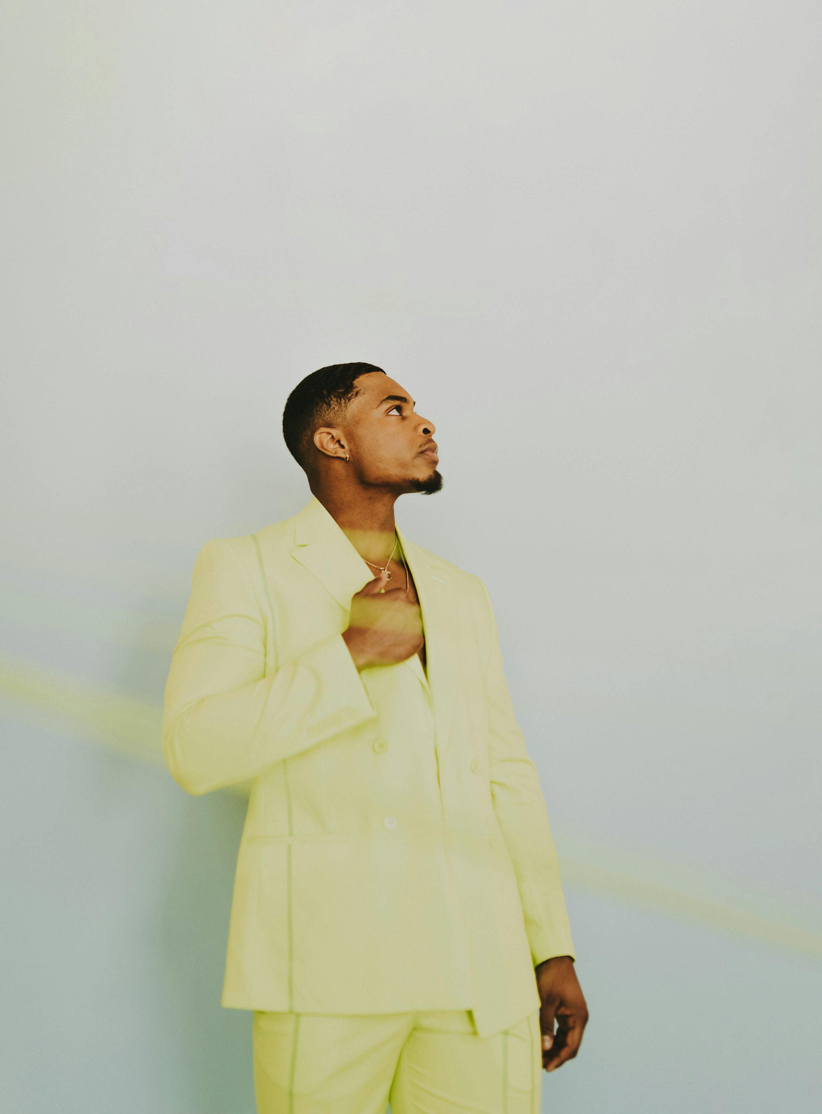 Young man in a trendy yellow suit posing elegantly against a white background.