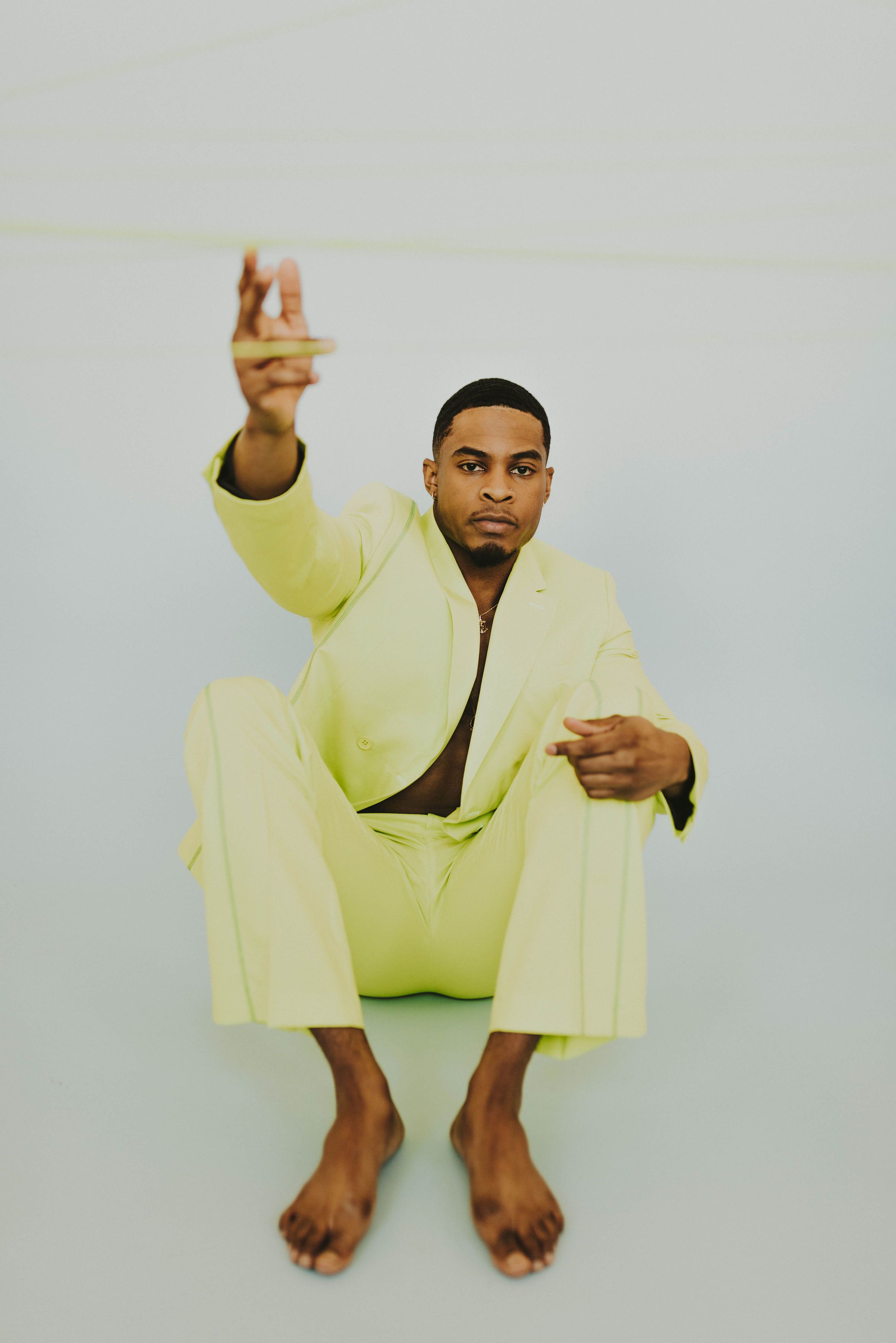 A confident man poses barefoot in a vibrant yellow suit during a studio shoot.