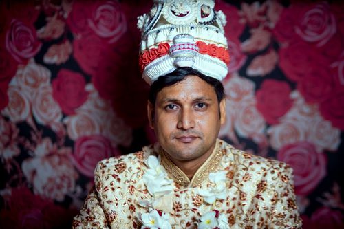 Free Indian groom in traditional attire with ornate headwear against floral backdrop. Stock Photo