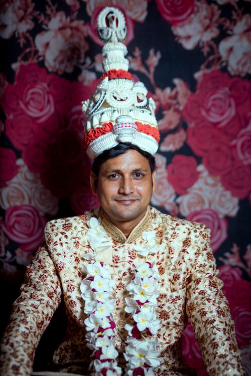 Free Portrait of a man wearing a traditional Indian groom outfit with elaborate headdress against floral backdrop. Stock Photo
