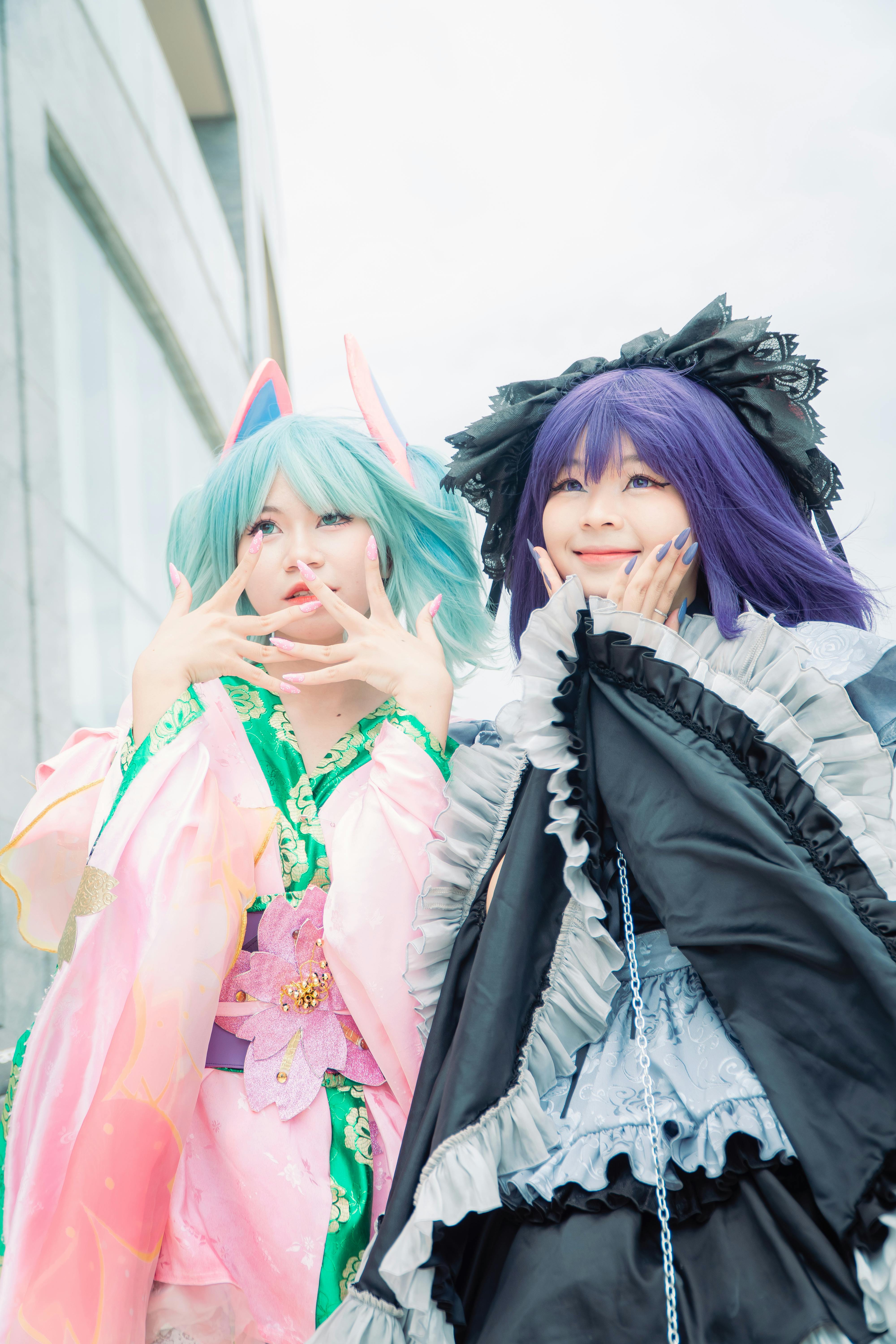 Two women in vibrant cosplay costumes with blue and purple hair.
