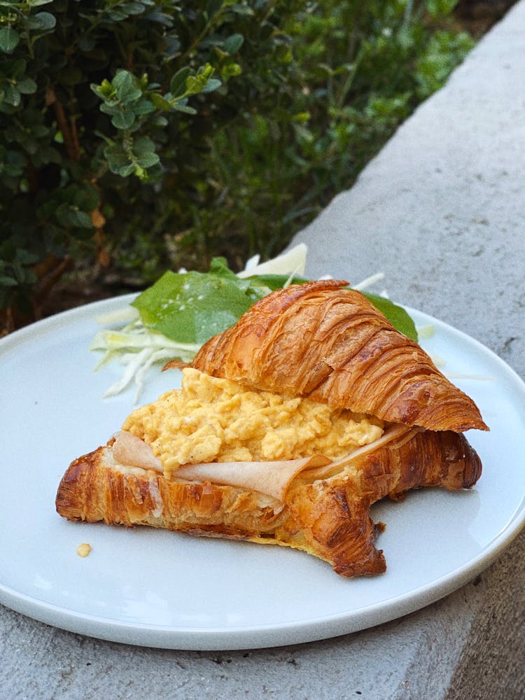 A Croissant With Scrambled Egg On A Ceramic Plate