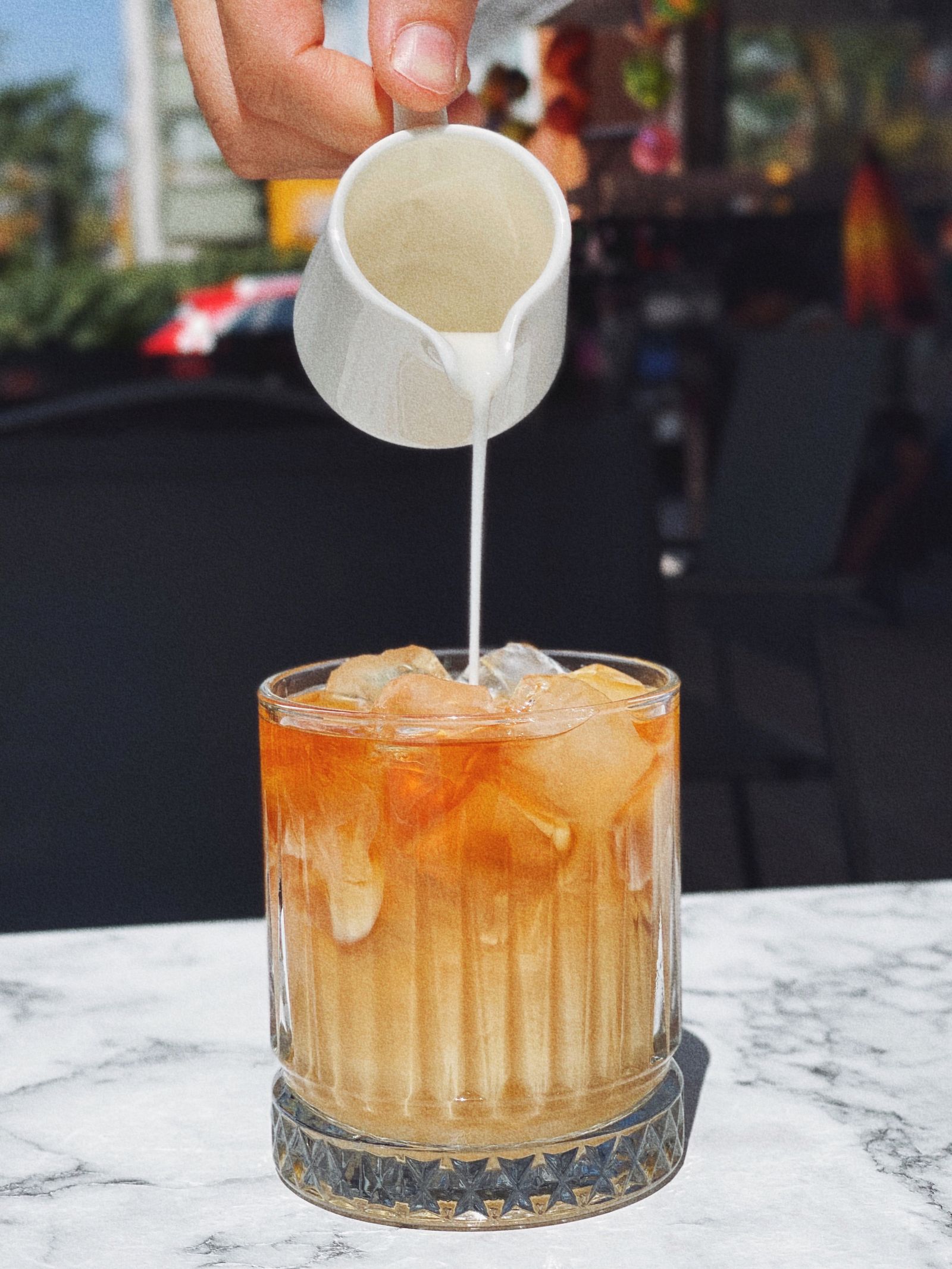 Milk being poured from a small white pitcher into amber iced tea