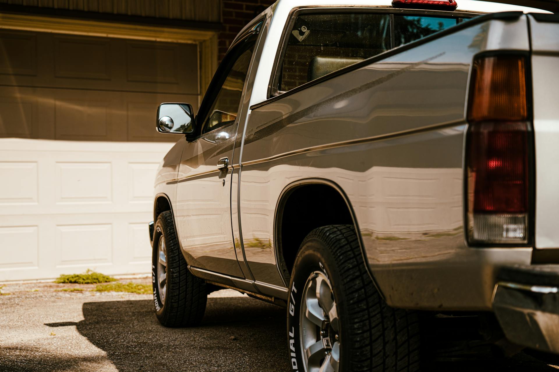 A silver pickup truck parked in a sunny residential driveway with closed garage doors.