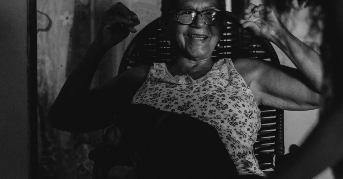 A joyful senior woman with eyeglasses enjoys a relaxed moment indoors, captured in monochrome.