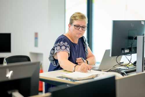 Free Professional woman wearing eyeglasses working at an office desk with a laptop and notebook. Stock Photo