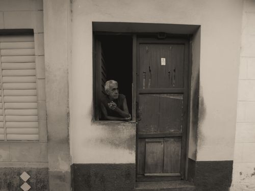Free Black and white photo of an elderly man smoking by the door in a rustic building. Stock Photo