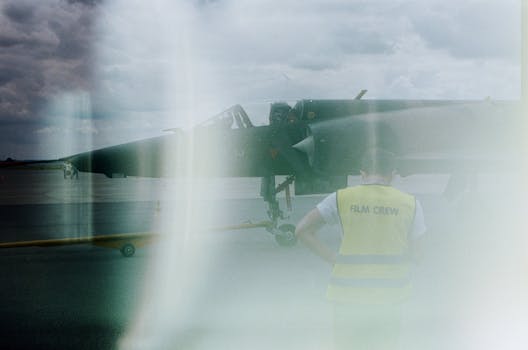 Film crew observes a military aircraft through a misty lens on an airport runway.