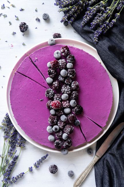 Top view of a vibrant purple cake adorned with frozen berries and lavender sprigs, perfect for dessert inspiration.
