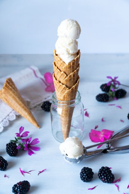 Delicious vanilla ice cream in cones with blackberries and flowers against a light background.