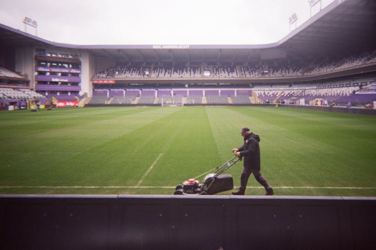 Man Mowing Grass In An Empty Soccer Stadium