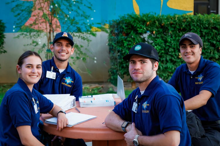 Students Wearing Blue T-shirts And Caps Posing By A Table