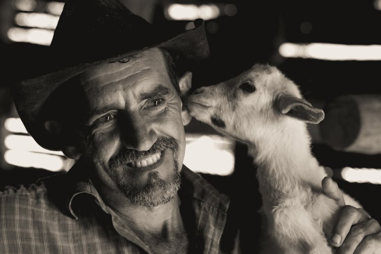 Sepia Toned Photo Of A Smiling Farmer With A Baby Goat