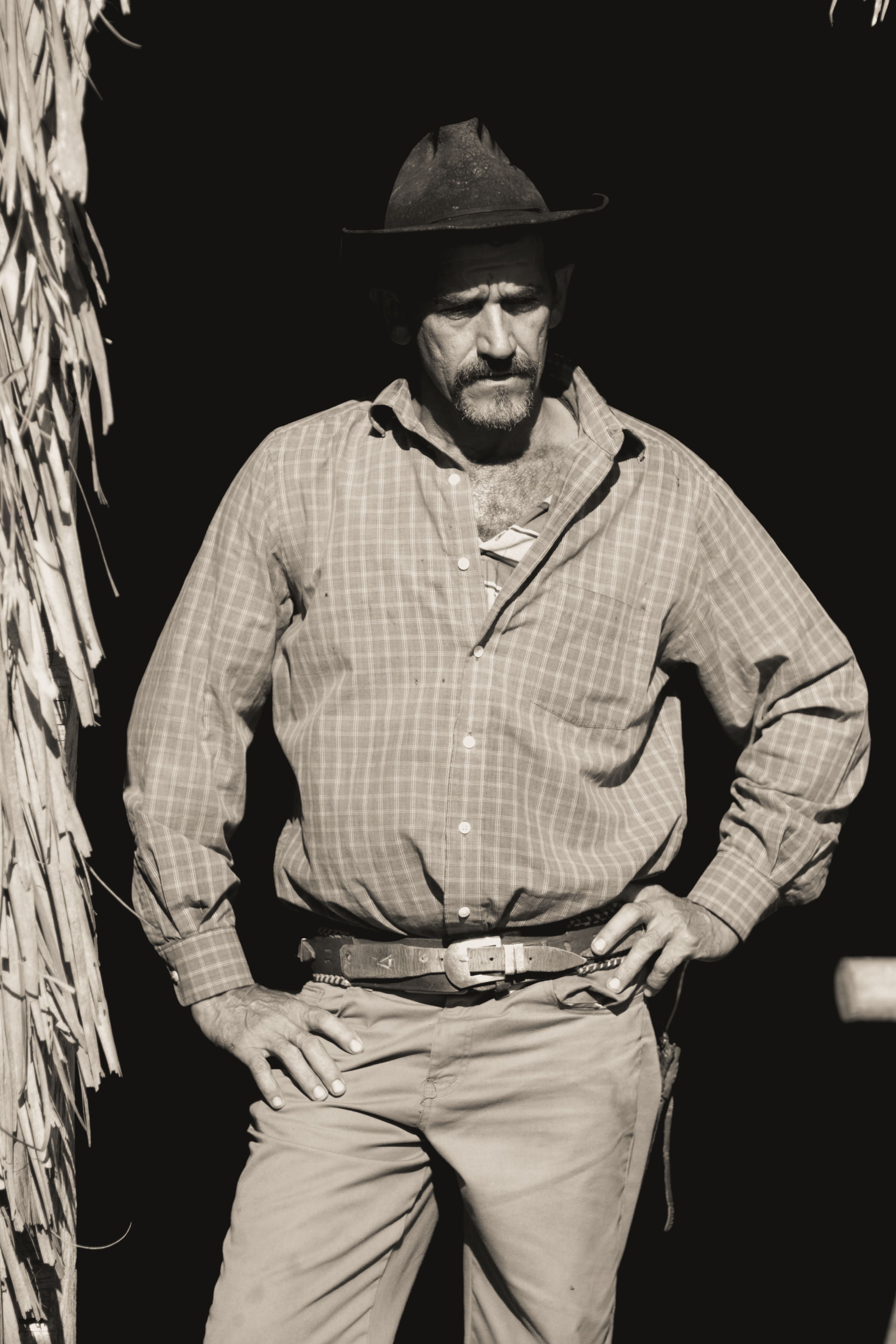 Grayscale portrait of a cowboy with a hat and mustache, hands on waist.