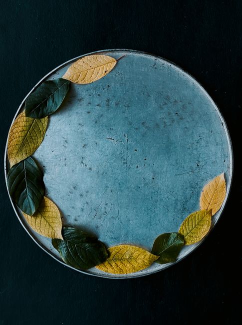 A top view of autumn leaves artfully arranged on a rustic metal plate, set against a dark background.
